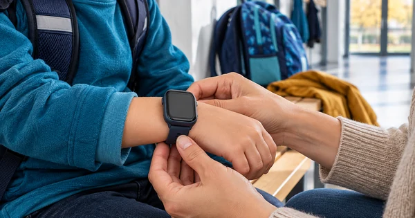 Un parent ajuste une montre connectée au poignet de son enfant près d’un cartable.